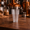 Stack of clear plastic cups on a wooden table with brewing equipment in the background